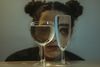 A young woman’s face seen through the refracted light of two different wine glasses.