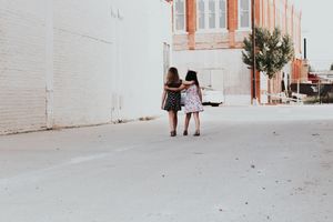 Two children, arm-in-arm, crossing a road.